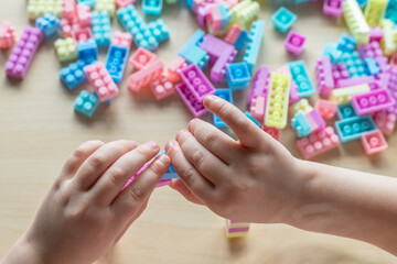 Small preschooler girl playing with colorful toy building blocks, sitting at the table.