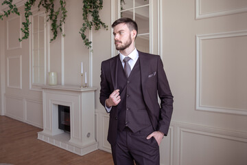 beautiful young man with a beard brunette model. guy in a classic suit in a light stylish interior.