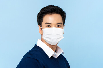 Close up portrait of young handsome Asian man wearing medical face mask isolated on light blue background - Powered by Adobe