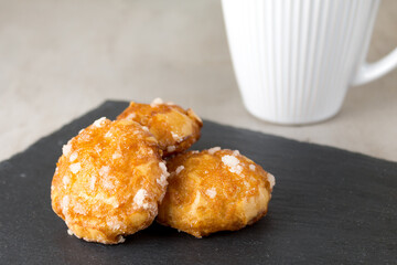 french chouquettes puffs with perles of sugar on black slate board with white cup of coffee. Classic French bakeries