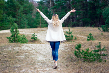 Fototapeta na wymiar One young beautiful blonde long haired woman with raised hands over green natural forest background outdoor.