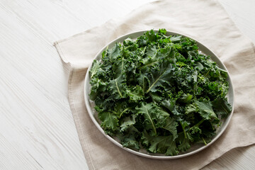 Raw Organic Baby Kale on a gray plate on a white wooden background, low angle view. Copy space.