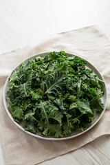 Raw Organic Baby Kale on a gray plate on a white wooden background, low angle view. Space for text.