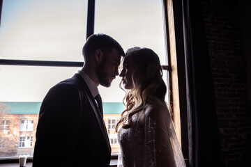 Silhouetted portrait of a bride and groom standing in front of a lacy window.