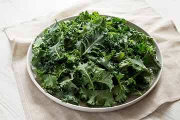 Raw Organic Baby Kale on a gray plate on a white wooden background, side view.