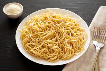 Homemade Cacio E Pepe Pasta with Pecorino Romano and Pepper on a white plate on a black background, low angle view.