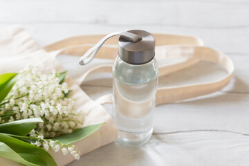 Zero waste concept. Glass water bottles and eco bag on a white wooden table.