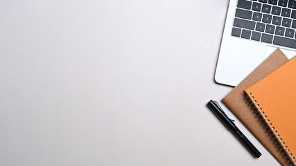 Top view of laptop computer, notebook and pen on white table.