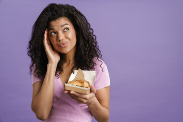 Young black woman looking upward while posing with hamburger