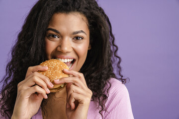 Young black woman with curly hair laughing while eating hamburger
