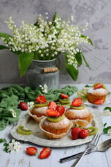 Vertical spring composition. Cupcakes with berries, a bouquet of lilies of the valley, green napkin on a gray rustic background