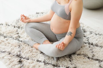Fototapeta na wymiar Beautiful pregnant woman sitting on yoga mat in living room, practicing meditation, young expectant lady doing sports at home, enjoying healthy lifestyle during pregnancy time, copy space