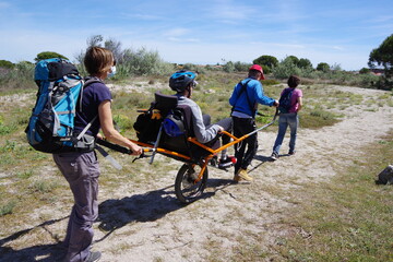 Randonnée dans la nature avec handicap avec joelette sorte de fauteuil roulant pour personne à mobilité réduite - obrazy, fototapety, plakaty