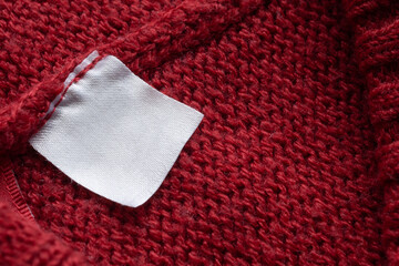 Blank laundry care clothes label on red knitted fabric texture background