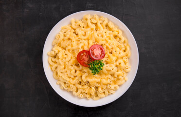 Macaroni and cheese on a white plate with parsley and cherry tomatoes on a black background