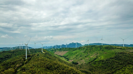 Fototapeta na wymiar Wind turbines on the green hilly terrain with the bright blue sky.