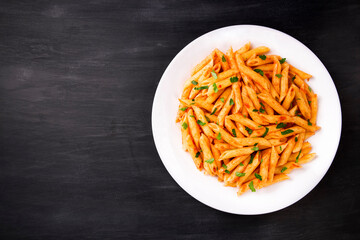 Penne pasta in tomato sauce, decorated with parsley on a black background