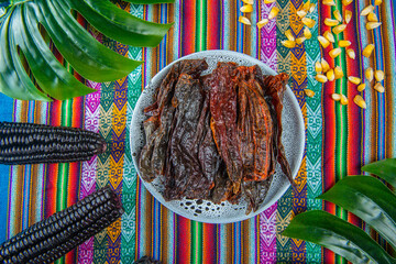 Dried red hot peppers in a blue dish on a colorful peruvian tablecloth 