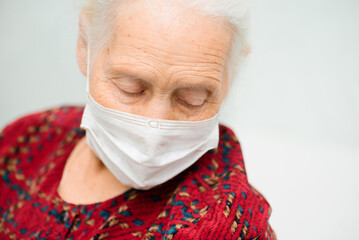 a large-faced portrait of an elderly woman with gray hair and sad eyes wearing a medical mask. Quarantine, disease, risk group, coronavirus infection.