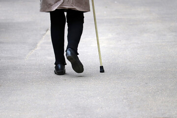 Woman walking with a cane on a street, female legs on sidewalk. Concept of disability, limping...
