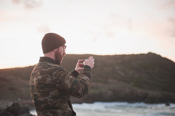 man by the sea taking pickture of the sunset with his phone