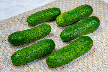 Six young green cucumbers on a beige wicker mat