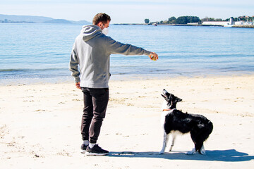 man in medical mask playing with his dog on the beach in the new normal