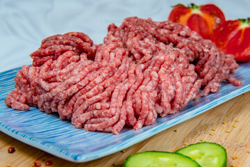 Freshly prepared ground beef in a rectangular blue plate with tomatoes and cucumbers aside