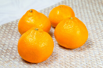 Four fresh tangerines on a beige wicker rug