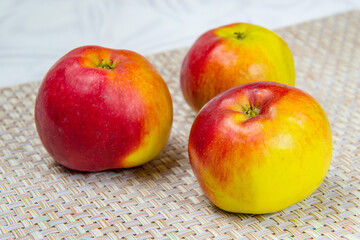 Three ripe apples on a beige wicker mat
