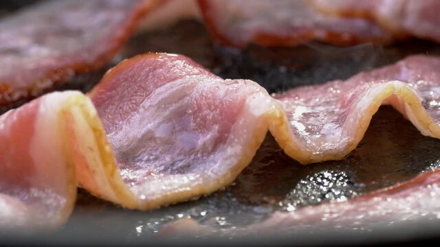Camera follows cooking bacon on grill. Shot with high speed camera. Slow Motion side view