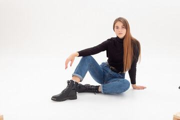 portrait of young attractive caucasian woman with long hair in black turtleneck, blue jeans isolated on white studio background. skinny pretty female sits on cyclorama. model tests of beautiful lady