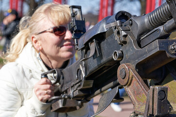 blonde woman in dark glasses shoots an anti-aircraft machine gun aiming upwards
