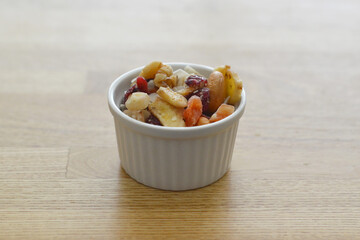 Mixed organic nuts and dried fruits in a ceramic cocotte on wooden surface