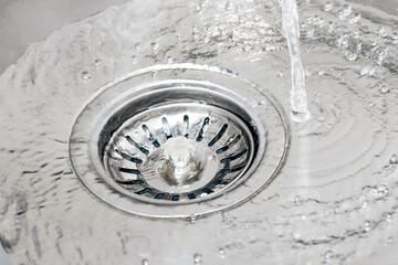 Water running from tap in a sink and pouring into drain with strainer stopper. - obrazy, fototapety, plakaty