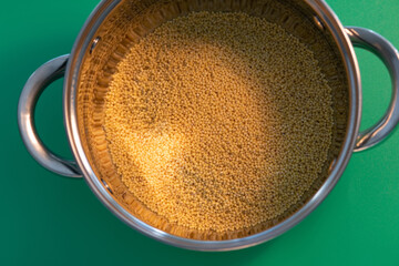 metal pan with millet for cooking. on the background of green.