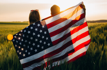 Image of young couple with the American flag in a wheat field at sunset. Independence Day, 4th of July.