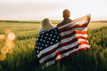 Patriotic holiday. Young couple with the American flag in a wheat field at sunset. Independence Day, 4th of July.
