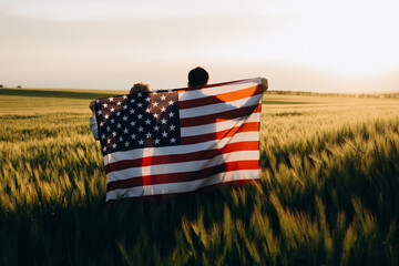 Image of young couple with the American flag in a wheat field at sunset. Independence Day, 4th of July.	