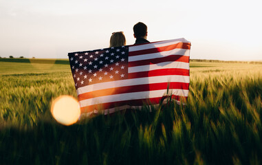 Image of young couple with the American flag in a wheat field at sunset. Independence Day, 4th of July.	