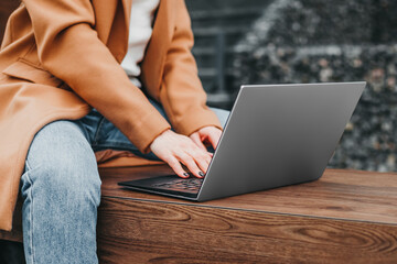Close up of a woman hands typing in a laptop in the street against the background of an office...