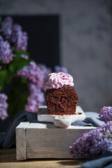 Chocolate sponge cake with berry cream on top. Beautiful still life - dessert with lilac flowers on rustic table. Food studio image, greeting card with copy space.