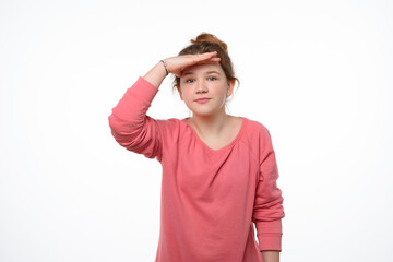 Portrait of a curious young girl looking far away with hand at her forehead, trying to see...