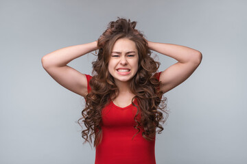 Fototapeta premium Depressed desperate young brunette woman in red t shirt, holding hands on hair, feeling pain in soul or being angry