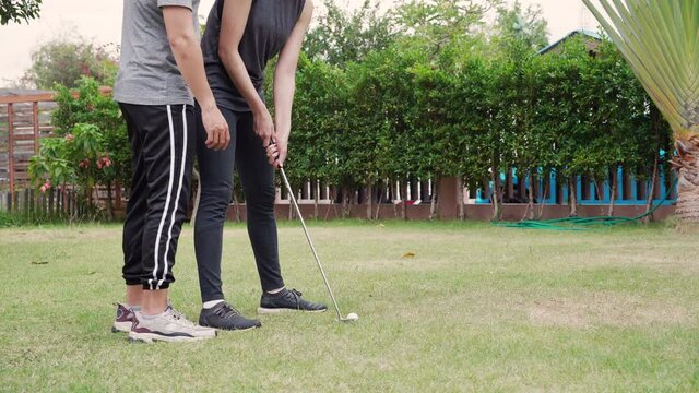 Asian young A couple training together to play golf on the behalf of the grass on vacation. Happy family sport concept