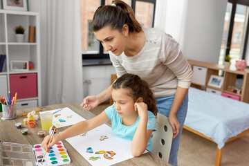 family, motherhood and leisure concept - mother spending time with her little daughter drawing or painting wooden chipboard items with colors at home