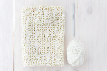 Knitted thing, crochet hook, skein of thread on a wooden table. Horizontal orientation, top view. 