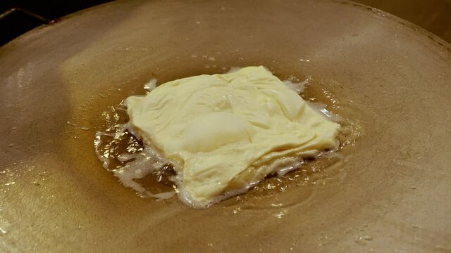 Close up, handheld shot of a raw Roti dought being fried in boiling oil in a hot pan, and flipped by unrecognizable local street food vendor. Local Asian food at night flea market concept.