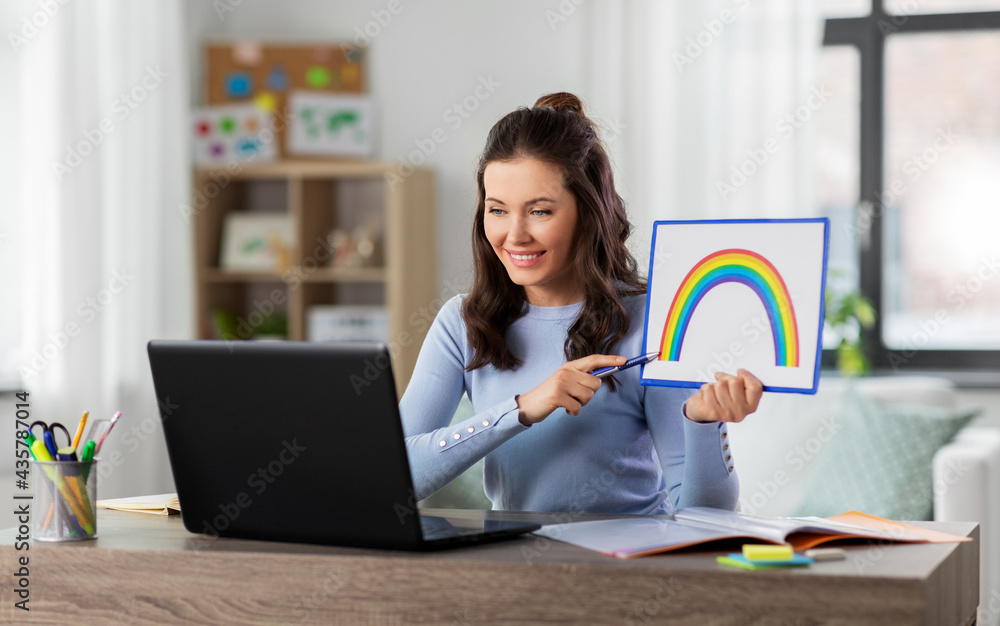 Wall mural distant education, school and people concept - happy smiling female teacher with laptop computer and picture of rainbow having online art class at home