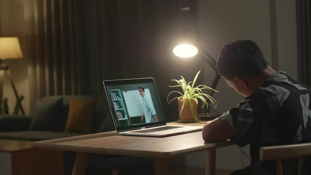 Asia Teen Boy Student Distance Learning With Online Teacher On Computer Screen From Home At Night
